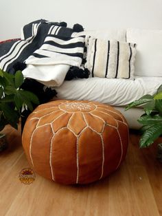 a large leather ottoman sitting on top of a wooden floor next to plants and pillows