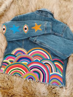 a pair of jean jackets with stars and rainbows painted on them sitting on top of a fur rug