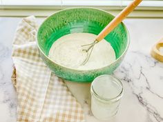 a green bowl filled with white liquid next to a wooden spoon on top of a counter