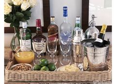 a wicker tray filled with liquor bottles and glasses next to lemons, limes, and nuts