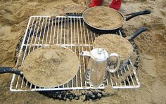 two pots and pans sitting on top of a metal grate in the sand