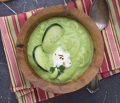 a wooden bowl filled with cucumber soup on top of a striped table cloth