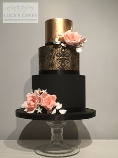 a three tiered black and gold wedding cake with pink roses on the top layer