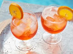 two glasses filled with orange juice and garnished with lemon wedges on a metal tray