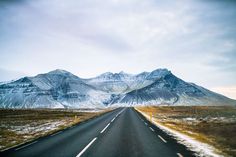 an empty road in the middle of nowhere with snow on the mountains and sky above