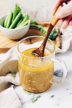 a person holding a wooden spoon in a glass mug filled with liquid and vegetables on a cutting board