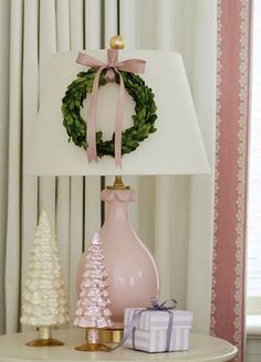 a lamp with a wreath on it sitting next to two small christmas trees