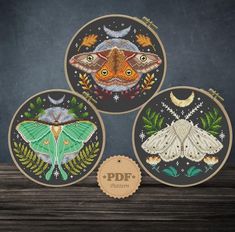 three embroidery kits with moths and leaves on them, one in the shape of a circle