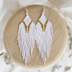 white and gold beaded fringe earrings on a wooden stand with feathers in the background