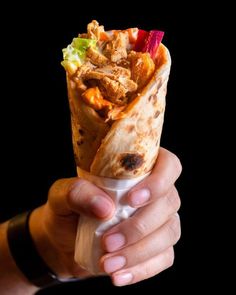 a hand holding a burrito filled with meat and veggies on top of it