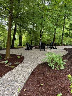 a gravel path in the middle of a forest with chairs and trees around it,