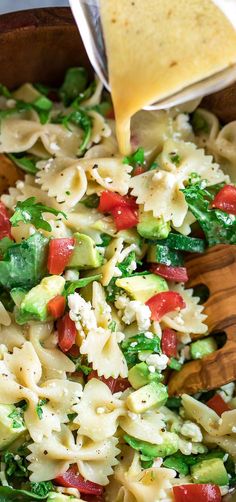 a wooden bowl filled with pasta and veggies being drizzled over it