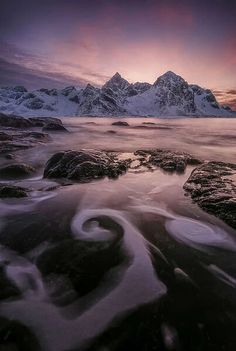 the sun is setting over some mountains in the distance, with water swirling around them