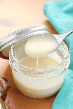 a glass jar filled with cream sitting on top of a wooden table next to a spoon