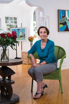 an older woman sitting in a green chair next to a table with flowers on it