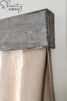 an old wooden frame hanging on the side of a wall next to a curtain rod