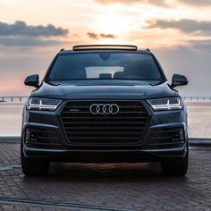 the front end of an audi suv parked in front of a body of water at sunset