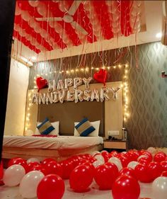 red and white balloons are floating in the air near a bed with a happy anniversary sign on it