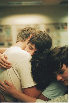 three young men hugging each other in a room