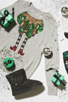 a christmas sweater with green and silver decorations on it, next to other holiday items