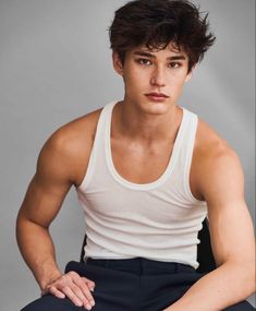 a young man sitting on top of a chair wearing a white tank top and black pants