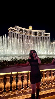 a woman standing in front of a fountain at night with her hands on her head