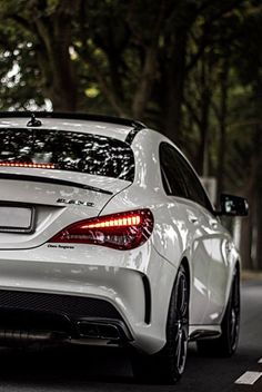 the rear end of a white mercedes cla parked in front of a tree lined street