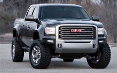 the front end of a silver truck parked on top of a parking lot with trees in the background