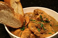 a bowl filled with meat and gravy next to a piece of bread