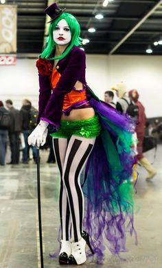 a woman dressed up as a clown with green hair and makeup, holding a cane