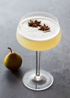 an alcoholic drink in a martini glass next to a pear