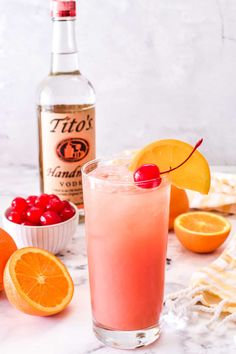 a pink drink with oranges and cranberries next to it on a marble surface