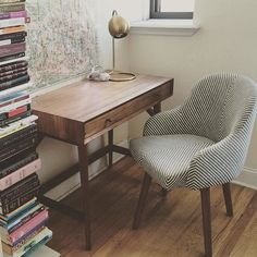 a chair sitting next to a desk with books on it and a window in the background