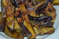 cooked eggplant and other vegetables on a white plate with seasoning over them