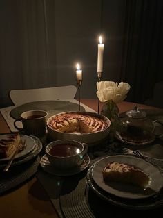 a table topped with plates and bowls filled with food next to two lit candles on top of each plate