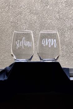 two wine glasses sitting on top of a table next to each other in front of a wall