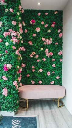 a pink bench sitting in front of a green wall with flowers growing on it's sides