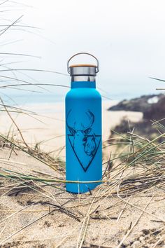 a blue water bottle sitting on top of a sandy beach next to grass and sand