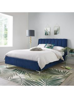 a blue bed with white sheets and pillows in a bedroom next to a large window