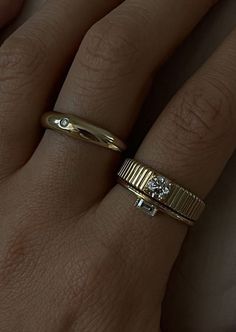 a woman's hand with two gold rings on top of her finger and one diamond ring in the middle