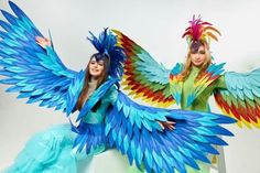 two women dressed in colorful costumes with large wings on their heads and arms, posing for the camera