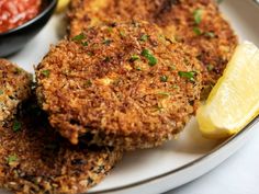 three crab cakes on a plate with lemon wedges