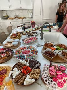 people standing around a table filled with different types of snacks and desserts on plates