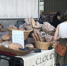 people are standing around a table with breads and pastries on it at an outdoor market