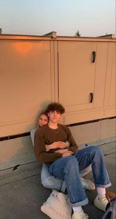 two people sitting on a bench with their arms around each other and one person leaning against the wall