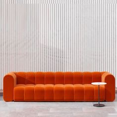 an orange couch sitting in front of a white wall with vertical striped walls behind it