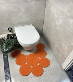 an orange bathroom rug is on the floor next to a toilet and potted plant