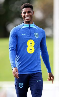 a young man smiles as he walks on the field wearing blue and yellow soccer uniforms