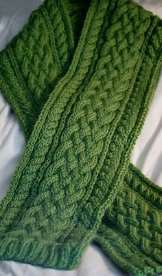 two green knitted scarves laying on top of a bed