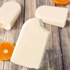 an orange and white popsicle sitting on top of a wooden table next to sliced oranges